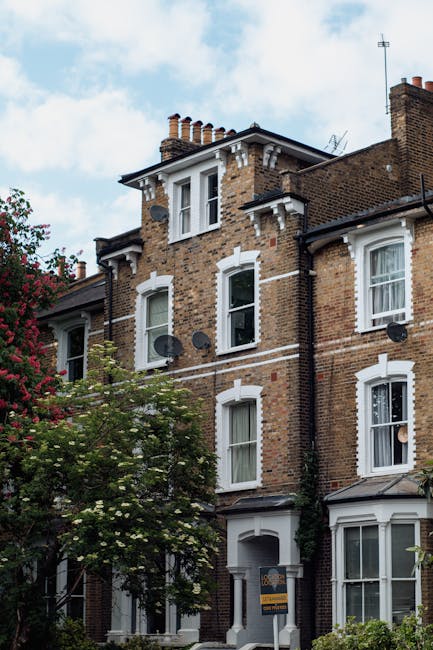 A row of Victorian-style terraced houses in South Acton with decorative ironwork balconies, large bay windows, and brick facades. The houses are built on a slight incline with front gardens enclosed b